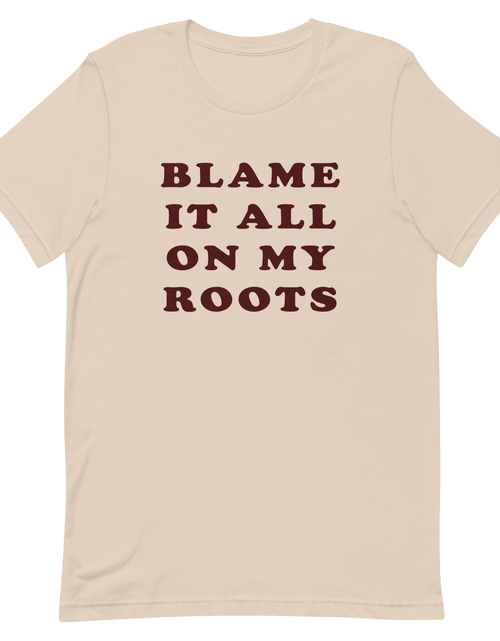 Load image into Gallery viewer, Beige t-shirt, front view, with a caption of blame it all on my roots. This is a lyric from the Garth Brooks song, friends in low places.

